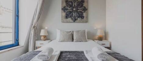 A neatly made bed with folded towels, a decorative wall piece, and two bedside lamps.