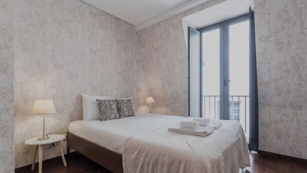 A bedroom with a bed, two bedside lamps, a round nightstand, a balcony with a railing, and a view of the sky. - Tagus View Penthouse · Triplex with Private Terrace (Lisboa)