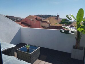 A rooftop terrace with a wicker table, a potted plant, and a view of buildings in the distance. - Tagus View Penthouse · Triplex with Private Terrace (Lisboa)