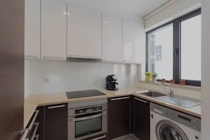A modern kitchen with white cabinets, a coffee maker, a sink, and a built-in washing machine. - Tagus View Penthouse · Triplex with Private Terrace (Lisboa)