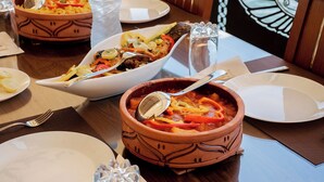 A dining table with various dishes, including a bowl of stew and a plate of food, set on a wooden table with a placemat. - Prince Anoush Dahabiya 3 Nights (Luxor)