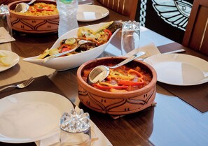 Una mesa de comedor con varios platos, incluyendo un tazón de estofado y un plato de comida, sobre una mesa de madera con un mantel individual.