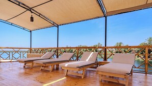 A covered outdoor area with wooden flooring and three lounge chairs. - Prince Anoush Dahabiya 3 Nights (Luxor)