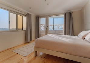 A bedroom with a large bed, a view through a sliding door to an outdoor balcony, and a wooden floor. - Prince Anoush Dahabiya 3 Nights  (Luxor)