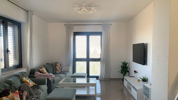 Una sala de estar moderna con un sofá, un reposapiés, una mesa de centro y un televisor montado en la pared.