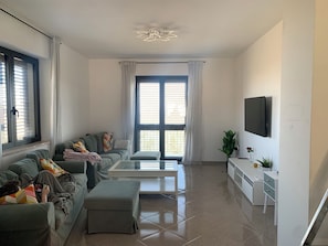 Ein modernes Wohnzimmer mit einer Couch, einem Hocker, einem Couchtisch und einem an der Wand montierten Fernseher.