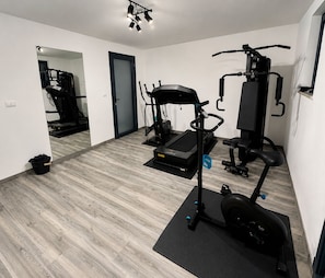 Ein kleines Fitnessstudio mit Laufband, Crosstrainer und einer Gewichtbank.