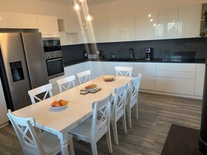 A modern kitchen with white cabinetry, a stainless steel refrigerator, a built-in oven, and a dining table with chairs. - Spacious 4-bed house in Archi, Italy-AC and fitness room sleeps 12 private pool (Archi)