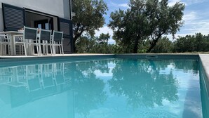 Una piscina con superficie azul cristalina, rodeada por un edificio moderno con balcón y mobiliario exterior.