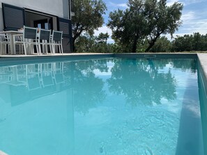 A swimming pool with a clear blue surface, surrounded by a modern building with a balcony and outdoor furniture. - Spacious 4-bed house in Archi, Italy-AC and fitness room sleeps 12 private pool (Archi)