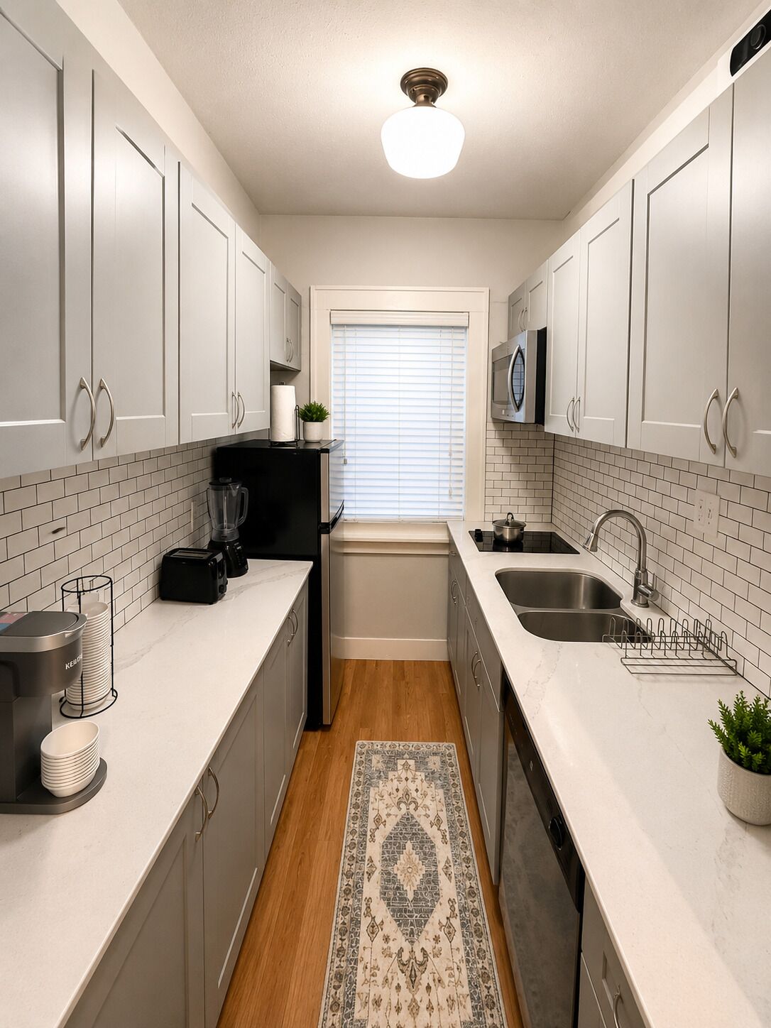 A modern kitchen with white cabinets, a black coffee maker, a kettle, and a microwave.