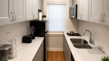 A modern kitchen with white cabinets, a black coffee maker, a kettle, and a microwave.