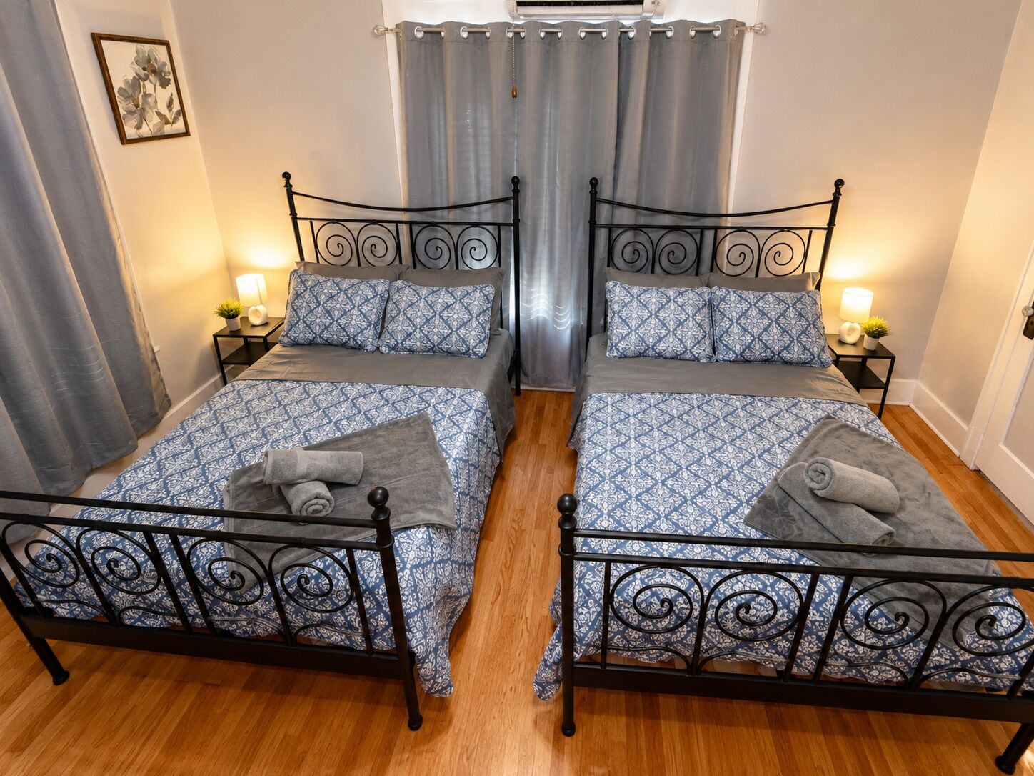 A double room with two beds, each with a patterned bedspread and pillows, a small bedside table with a lamp, and a curtain.