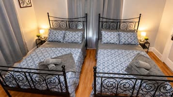 A double room with two beds, each with a patterned bedspread and pillows, a small bedside table with a lamp, and a curtain.