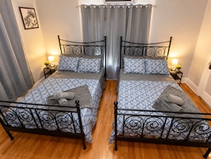 A double room with two beds, each with a patterned bedspread and pillows, a small bedside table with a lamp, and a curtain.