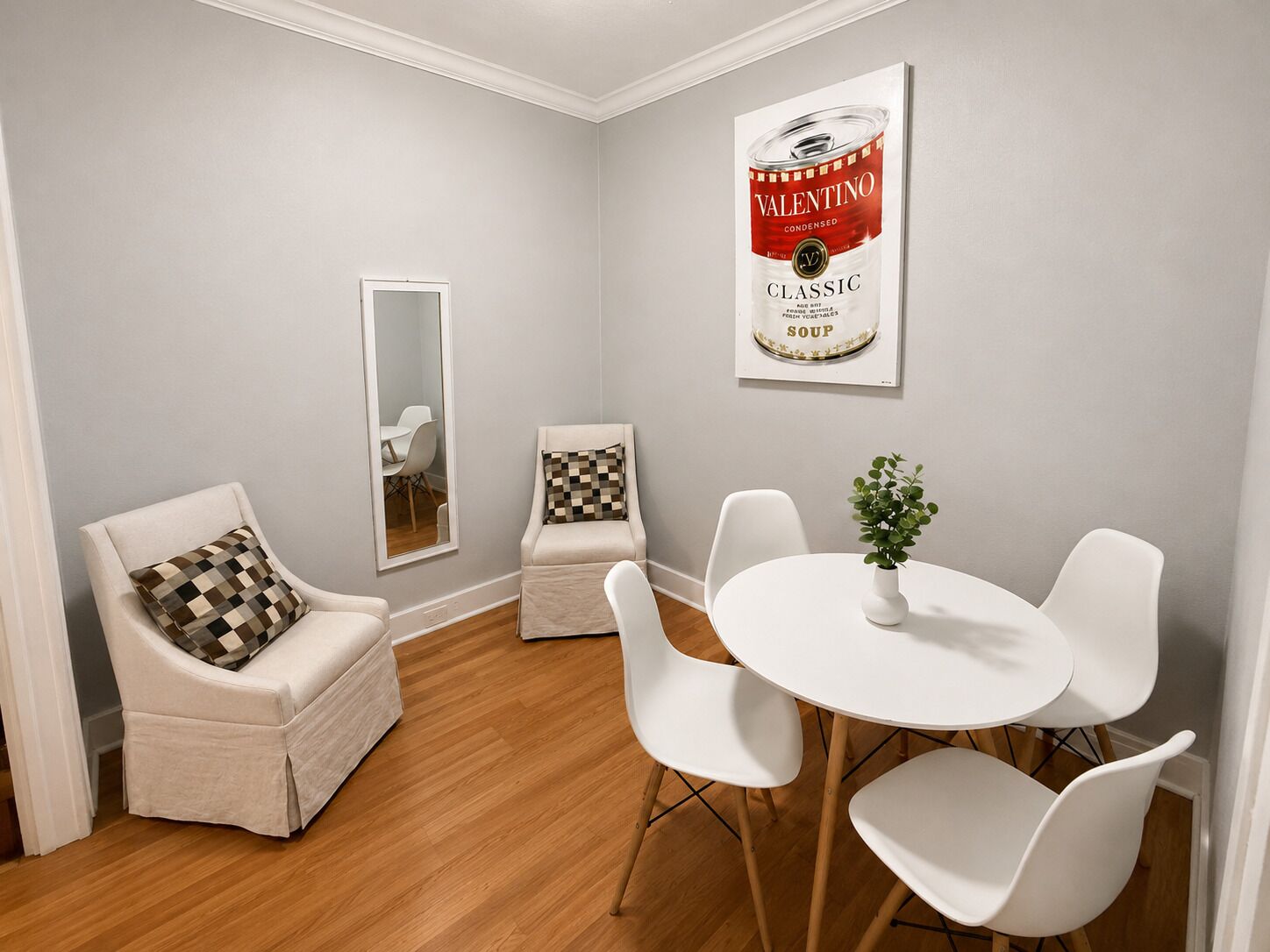 A dining area with a white table and chairs, a mirror, and a framed poster on the wall.
