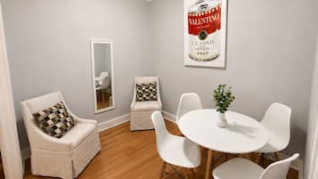 A dining area with a white table and chairs, a mirror, and a framed poster on the wall.