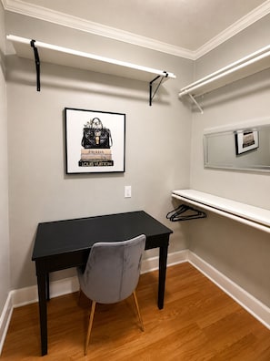 Ein Zimmer mit einem schwarzen Schreibtisch, einem grauen Stuhl, einem gerahmten Bild von Designertaschen und einem Spiegel an der Wand.