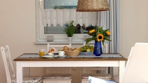 Una mesa de desayuno con huevos, tostadas y fruta, un florero con girasoles y una lámpara de mimbre.