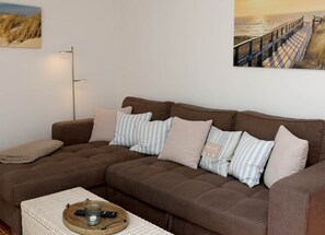 Ein braunes Sofa mit gestreiften und einfarbigen Kissen, einem Ablagetisch für die Fernbedienung sowie einem Bild von Strand und Steg.