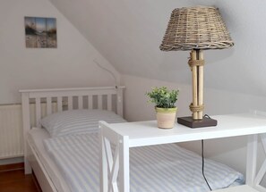 Ein Schlafzimmer mit einem weißen Bett, einem kleinen Tisch mit einer Lampe und einem Blumentopf.