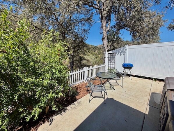 An outdoor patio with a table and chairs, a barbecue grill, and a white fence.