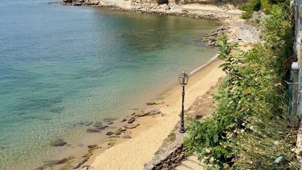 A coastal beach with clear water, a stone staircase, and a building on a hill in the background. - Break at Sea (Castellabate)