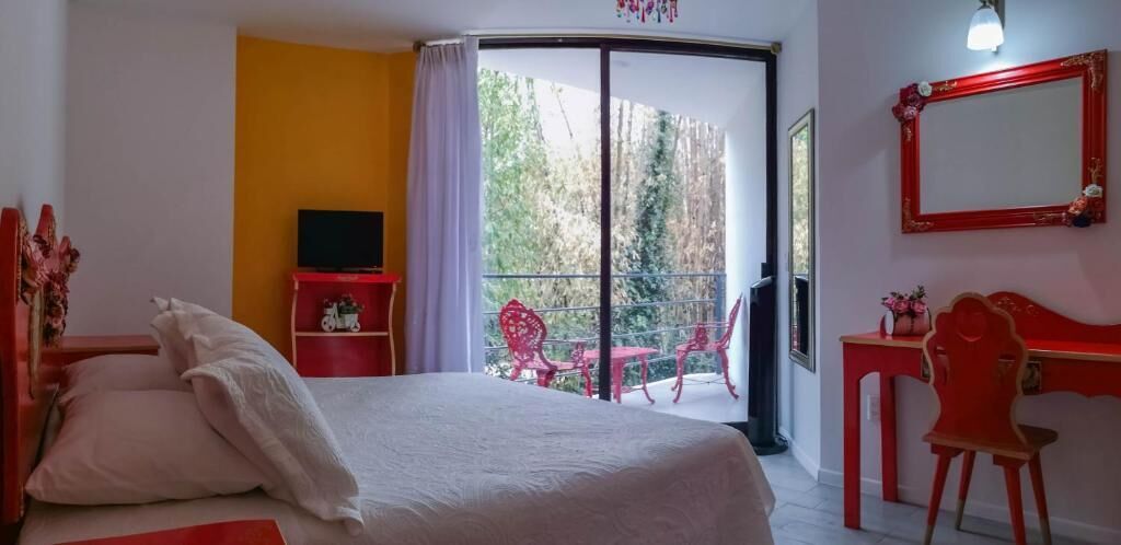 Une chambre avec un lit, un bureau, une chaise, une télévision et un balcon équipé de chaises.
