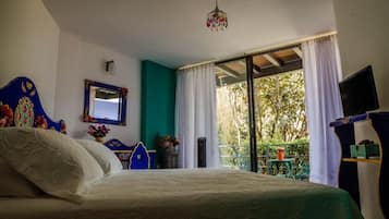 Une chambre à coucher avec un lit, un miroir, une télévision et un balcon donnant sur la forêt.