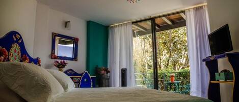 Una camera da letto con un letto, uno specchio, una televisione e un balcone con vista sugli alberi.