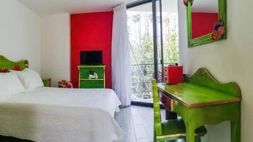 A bedroom with a bed, a green nightstand, a red wall, and a window with a view of greenery.