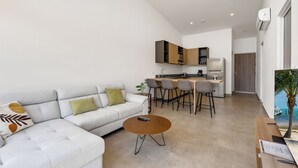 En moderne stue med sofa, sofabord og et køkkenområde med barstole.