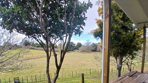 A wooden deck with a view of a grassy field and trees. - Beautiful and Private Farmstead Cabin, only 15min from the Taupo. (Taupō)