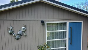 A single-story building with a blue door, a window with curtains, and a small porch with a potted plant. - Beautiful and Private Farmstead Cabin, only 15min from the Taupo. (Taupō)