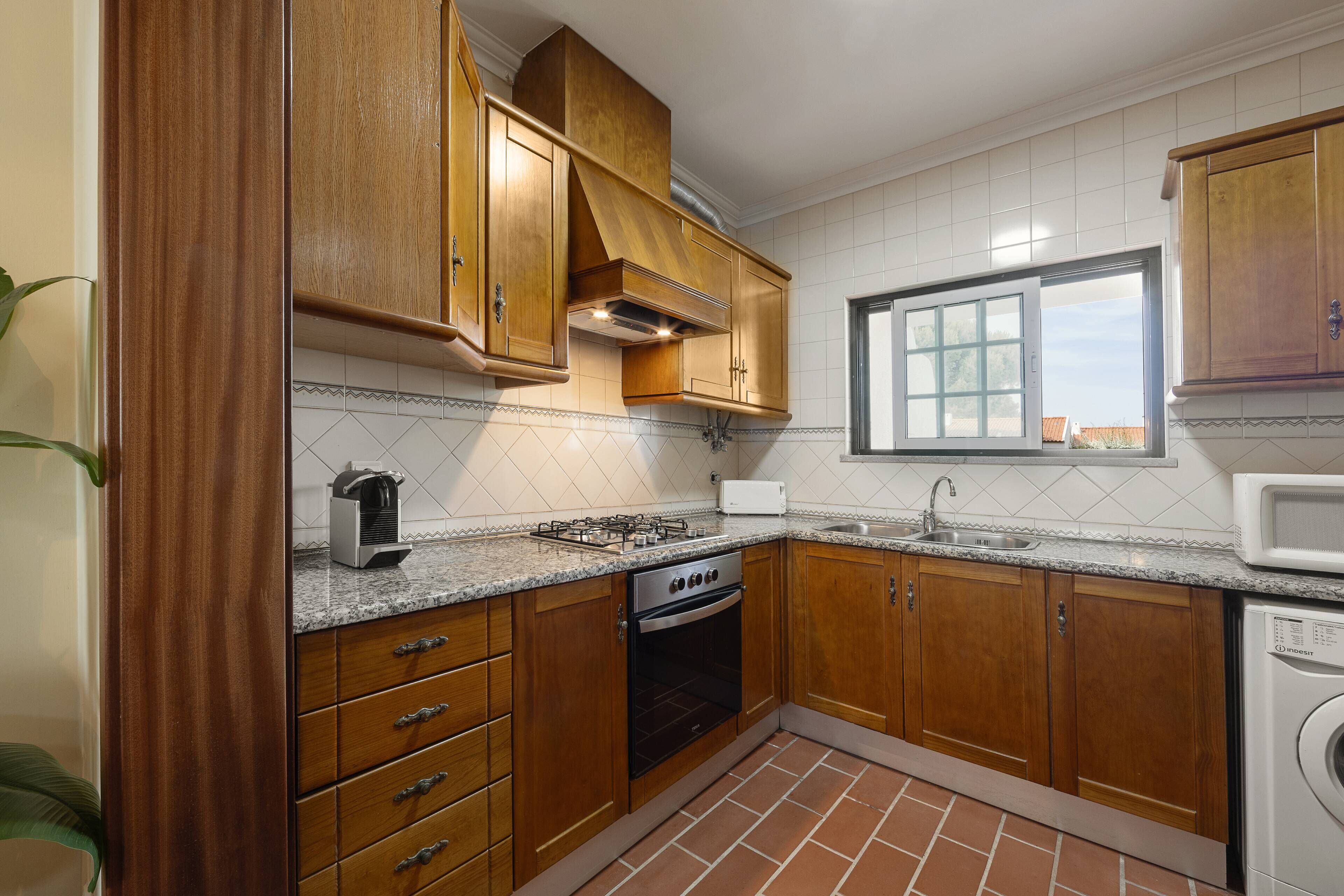 A kitchen with wooden cabinets, a gas stove, an oven, a microwave, and a washing machine.