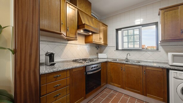 A kitchen with wooden cabinets, a gas stove, an oven, a microwave, and a washing machine. - Jardim da Lagoa - Rustic Retreat (Óbidos)
