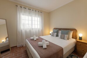 Ein Hotelzimmer mit Bett, Nachttisch, Spiegel, einem Fenster mit durchsichtigen Vorhängen und einem Dielenboden aus Ziegeln.