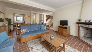 A living room with a sofa, coffee table, TV, fireplace, and a staircase leading to an upper level. - Jardim da Lagoa - Rustic Retreat (Óbidos)