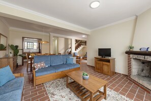 Ein Wohnzimmer mit Sofa, Couchtisch, Fernseher, Kamin und einer Treppe, die in eine obere Ebene führt.