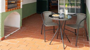An outdoor patio with a brick floor, a table with chairs, a brick oven, and a glass door leading to an interior space. - Jardim da Lagoa - Rustic Retreat (Óbidos)