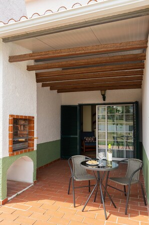 Eine Außenpatio mit Pflasterboden, einem Tisch mit Stühlen, einem Backofen aus Ziegeln und einer Glastür zu einem Innenbereich.