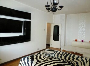Ett sovrum med ett sängöverkast i zebrastripe, en vit byrå, en spegel och en kristallkrona.