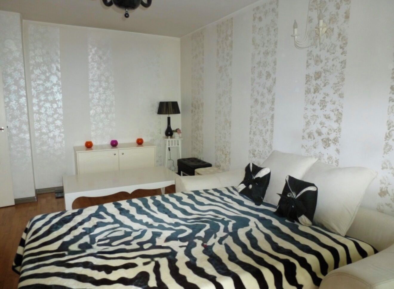 A bedroom with a zebra-patterned bedspread, a white sofa, a bedside table with a lamp, and a wardrobe with a mirror.