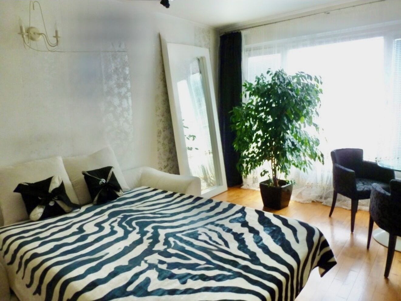 Une chambre à coucher avec une couvre-lit à motifs zébrés, une plante en pot, une chaise et une grande fenêtre.