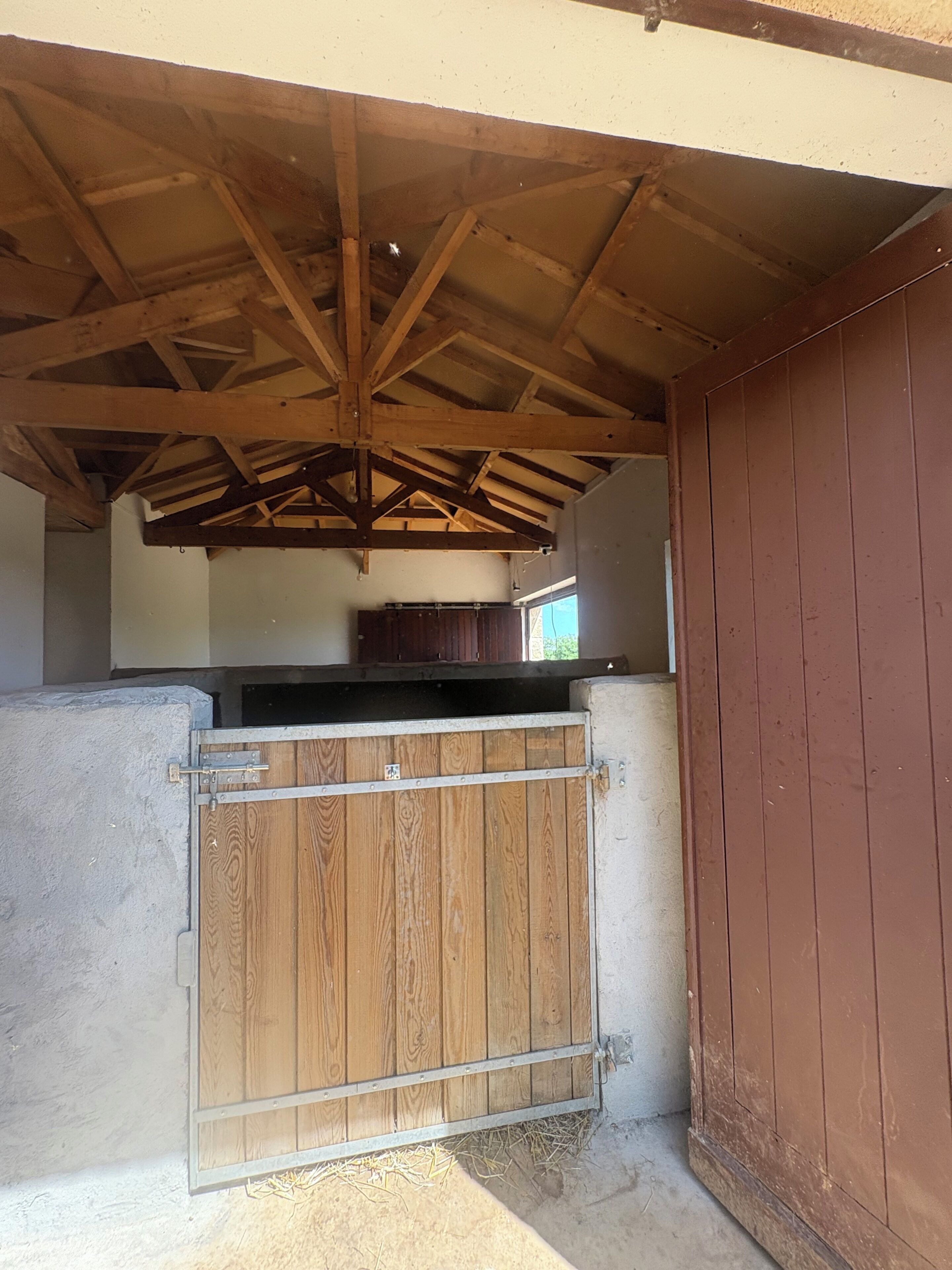 Un espacio al aire libre techado con techo de madera, una reja de metal y un muro de concreto.