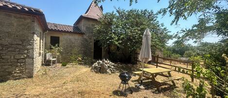 A stone building with a tiled roof, a wooden fence, and a grill in the yard.