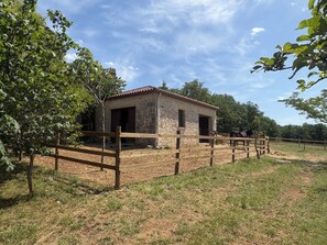 A stone building with a red-tiled roof, surrounded by a wooden fence, and two horses in the background. - Breathtaking stone house with a dovecote near the horses (Mauroux)