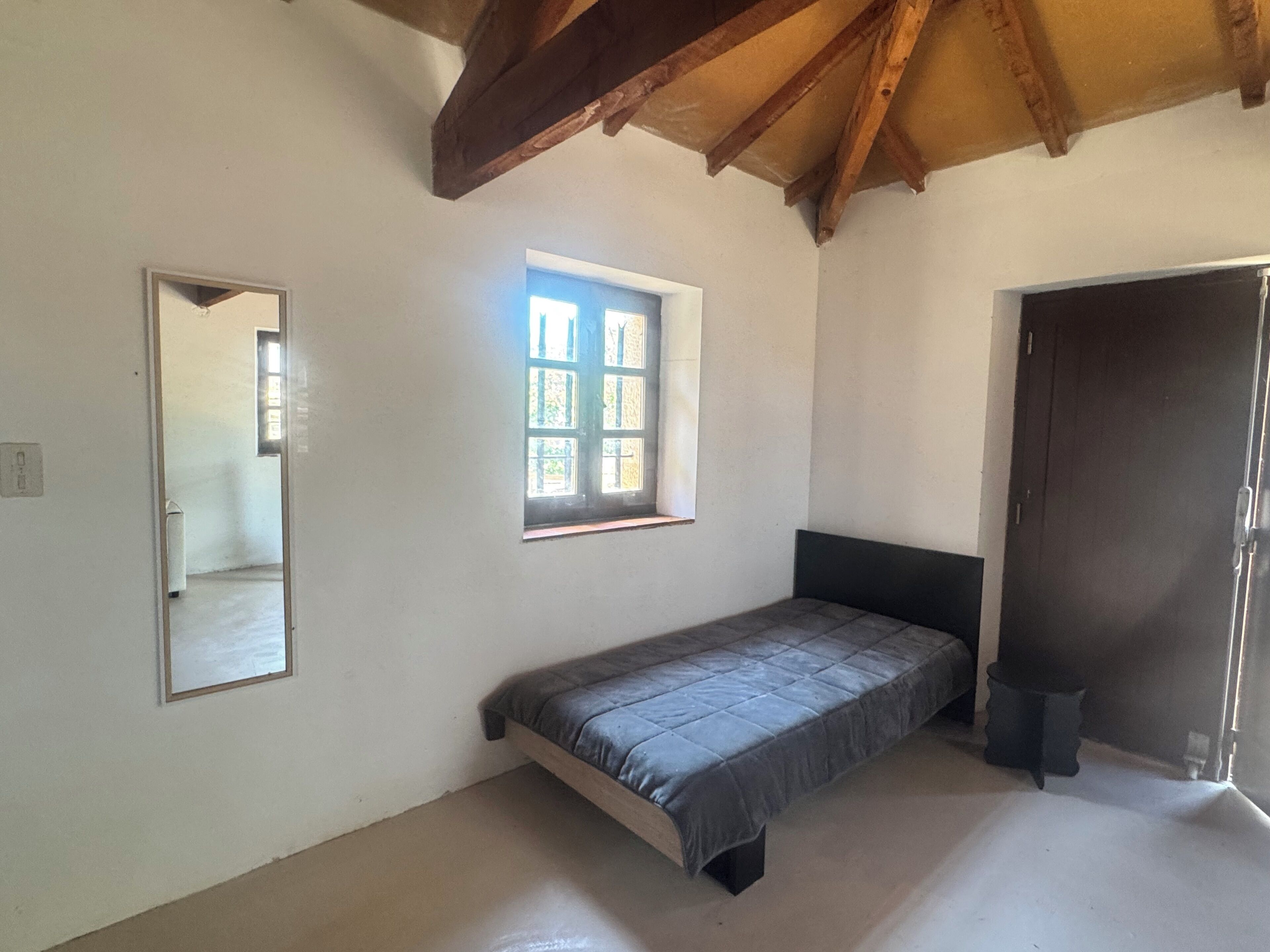 A bedroom with a bed, a window, a door, and a mirror.