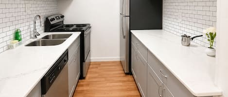 A compact kitchen with white cabinetry, a stainless steel sink, a microwave, a stove, and a refrigerator.