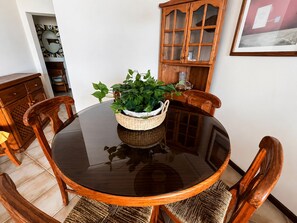 Una mesa redonda de madera con superficie de vidrio, rodeada de sillas de madera, y una cesta tejida con plantas verdes en el centro.